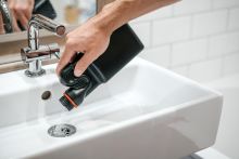 Picture of a person's hand pouring drain cleaner to unblock a washbasin.