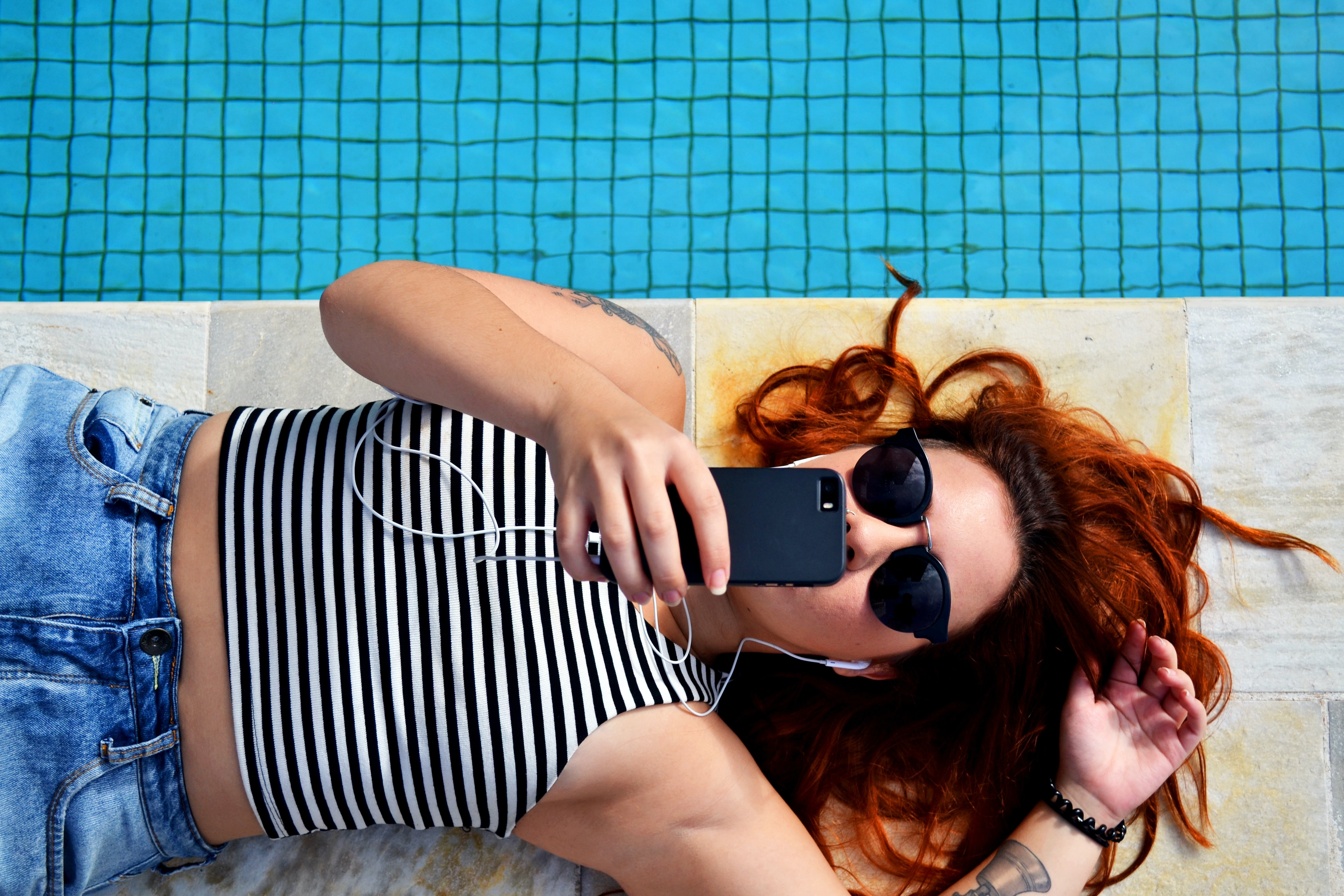 Young woman next to swimming pool, checking her phone