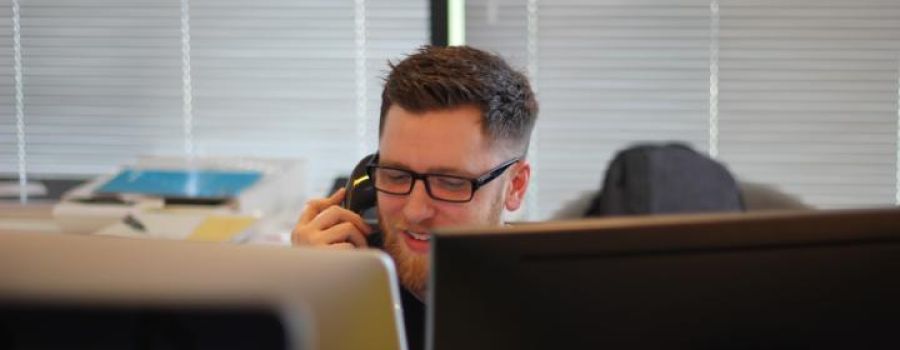 Man with glasses on the phone in front of computers